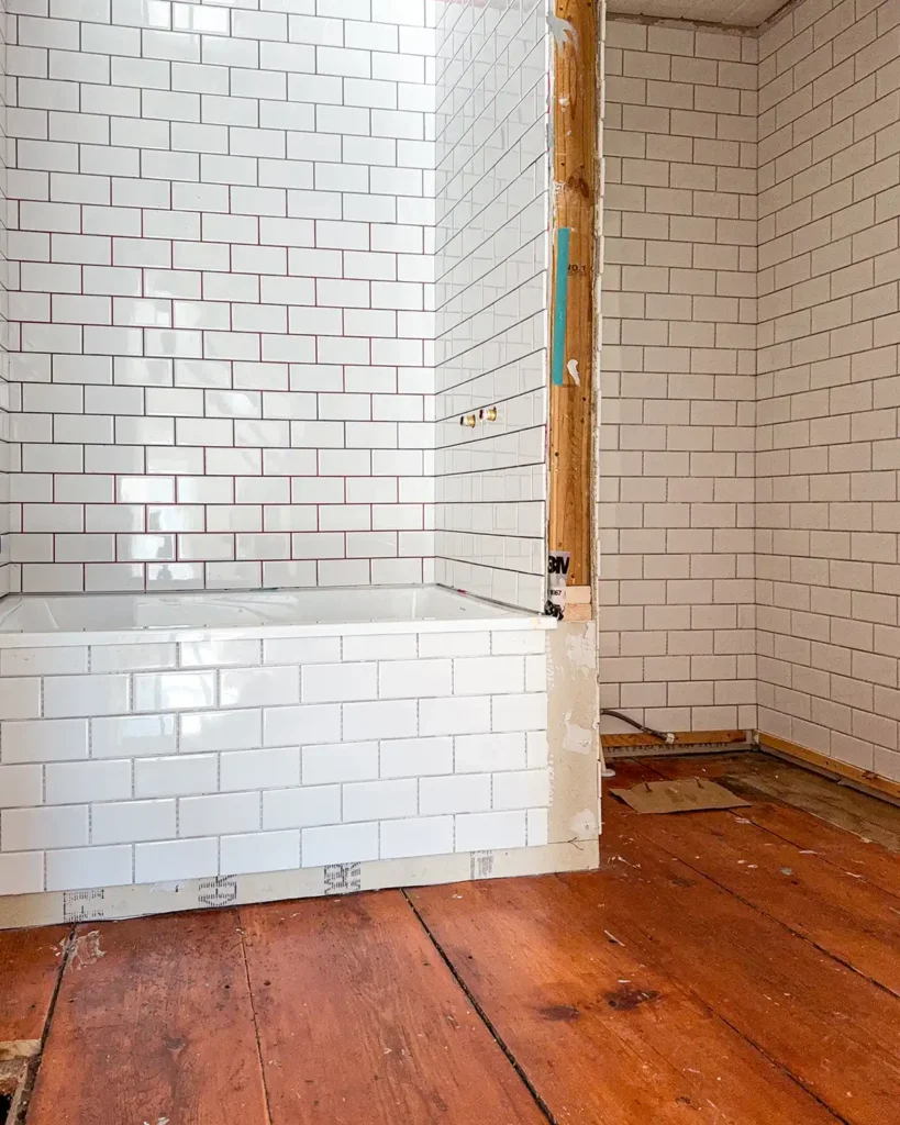 Subway tiling progress in a small bathroom with wide pine floors