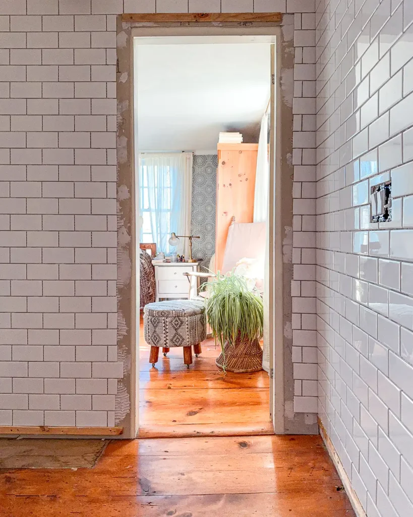 Tiling progress in a small bathroom renovation with wall-to-wall, floor-to-ceiling white subway tile installed, still need to grout the tiles and install trim