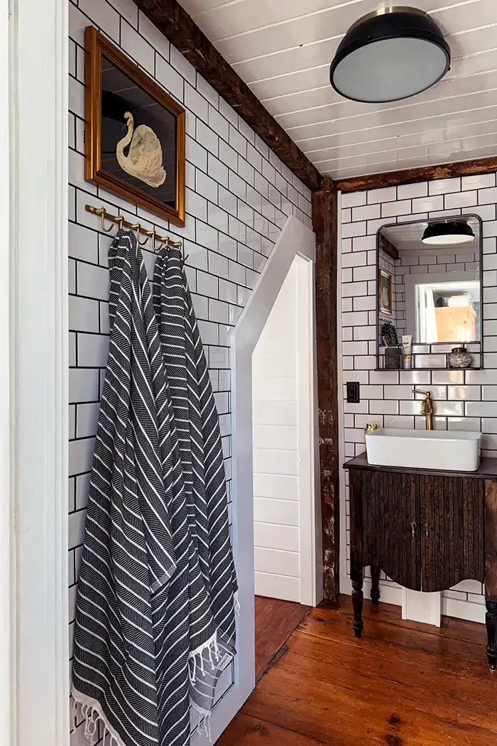 Finished bathroom renovation with wide pine floors, white subway tile with black grout, and a planked ceiling
