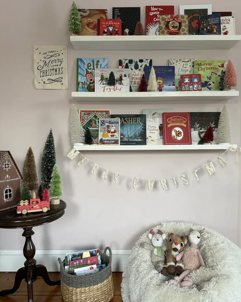 Kids Christmas bookshelves in their room with open shelves filled with Christmas picture books, decorated for Christmas with bottle brush trees and a merry Christmas banner. White furry bean bag underneath the bookshelves with reindeer stuffed animals.