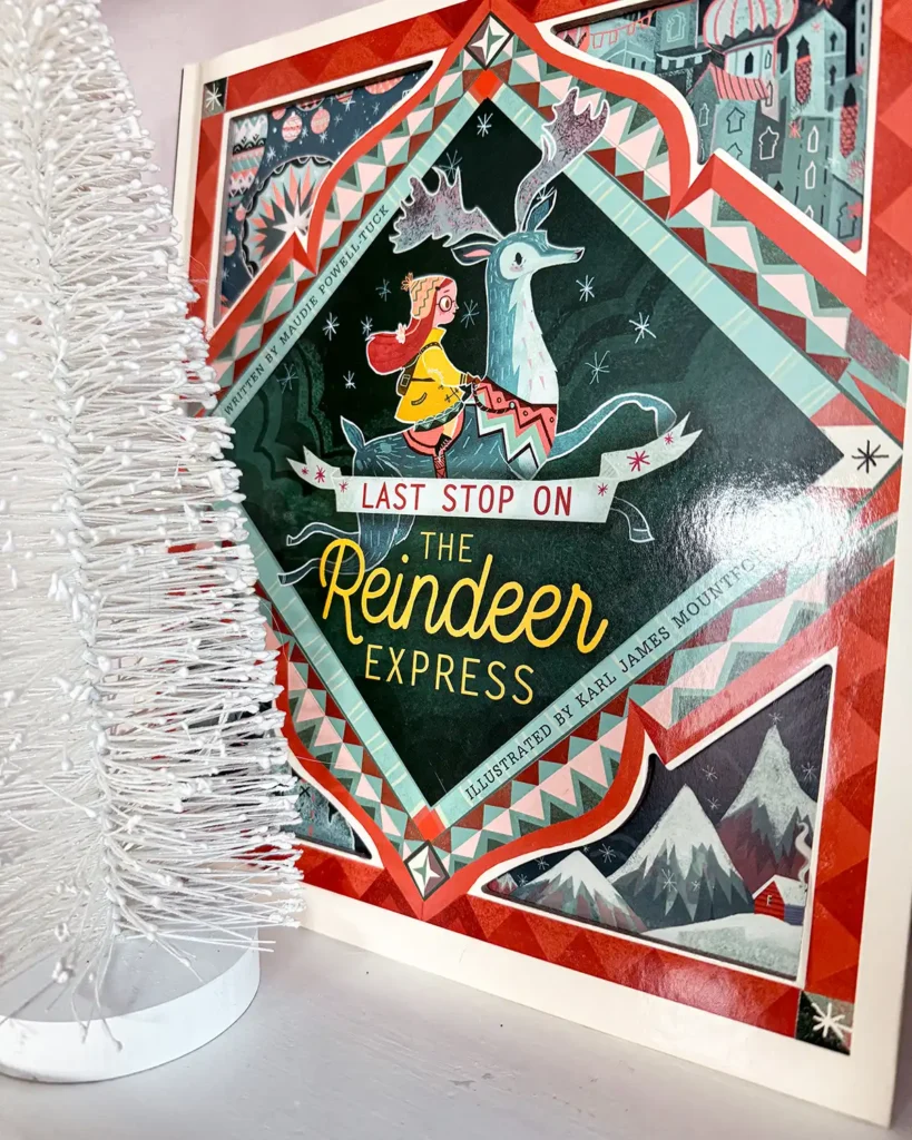 The Last Stop on the Reindeer Express picture book on an open shelf decorated for Christmas with bottle brush trees