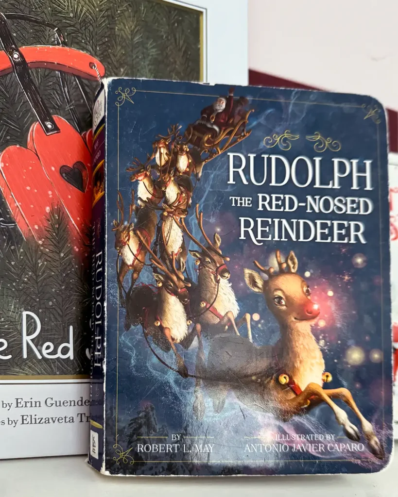 Rudolph board book on a kid's bookshelf filled with Christmas picture books