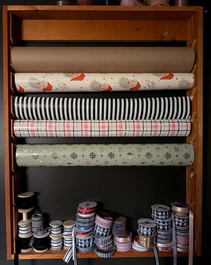 Wrapping paper on a wooden wrapping paper storage rack with piles of ribbon on the bottom shelf