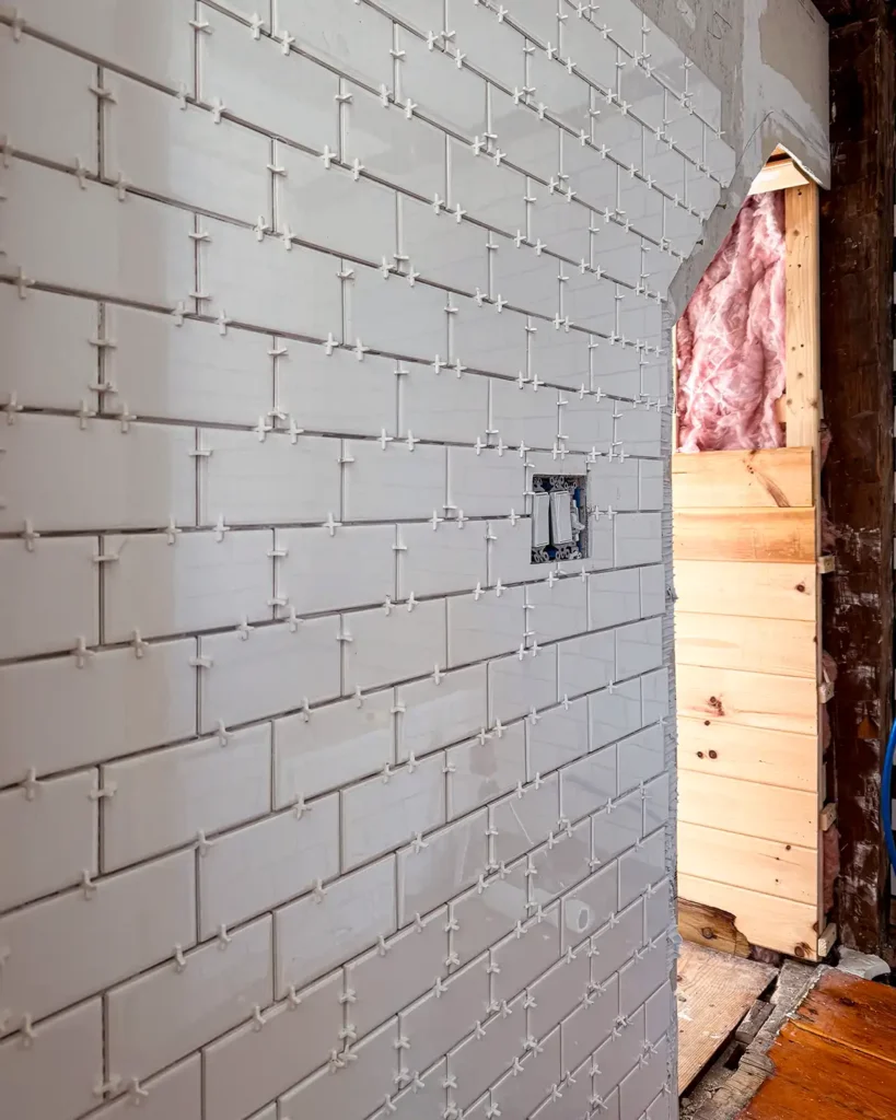 X-shaped tile spacers used for installing white subway tiles on bathroom walls