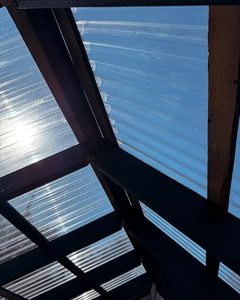 Plastic roof panels, a corrugated polycarbonate, installed on top of a greenhouse roof