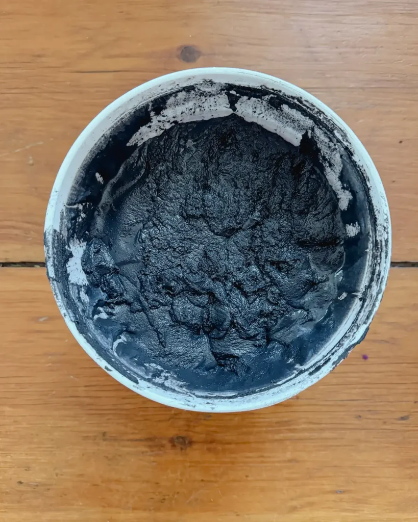 Open bucket of pre-mixed grout in black sitting on the floor