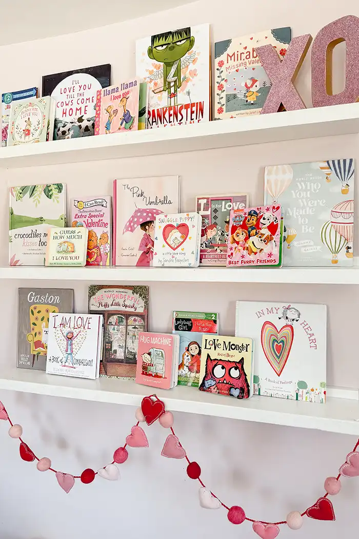 Valentines picture books for kids featured image with open shelves of Valentines Day books decorated with a felt heart garland