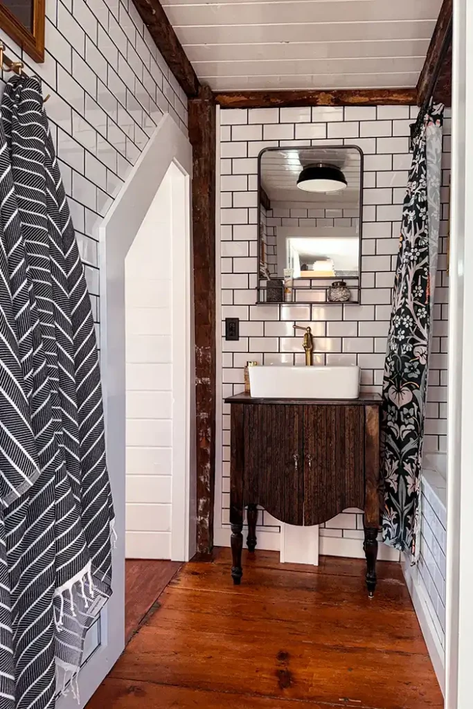 A low cost bathroom remodel budget breakdown featuring a gut remodel of a small bathroom with white subway tile, black grout, vintage floors, and a DIY vanity