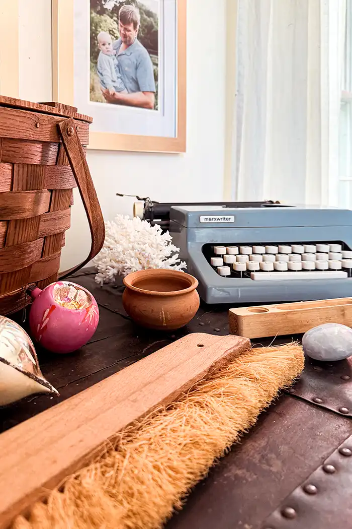 Treasures found at the May 2024 Brimfield flea market including a picnic basket, typewriter, Christmas ornaments, wallpaper brush, thermometer, terracotta pot, coral, and a blue calcite crystal palm stone
