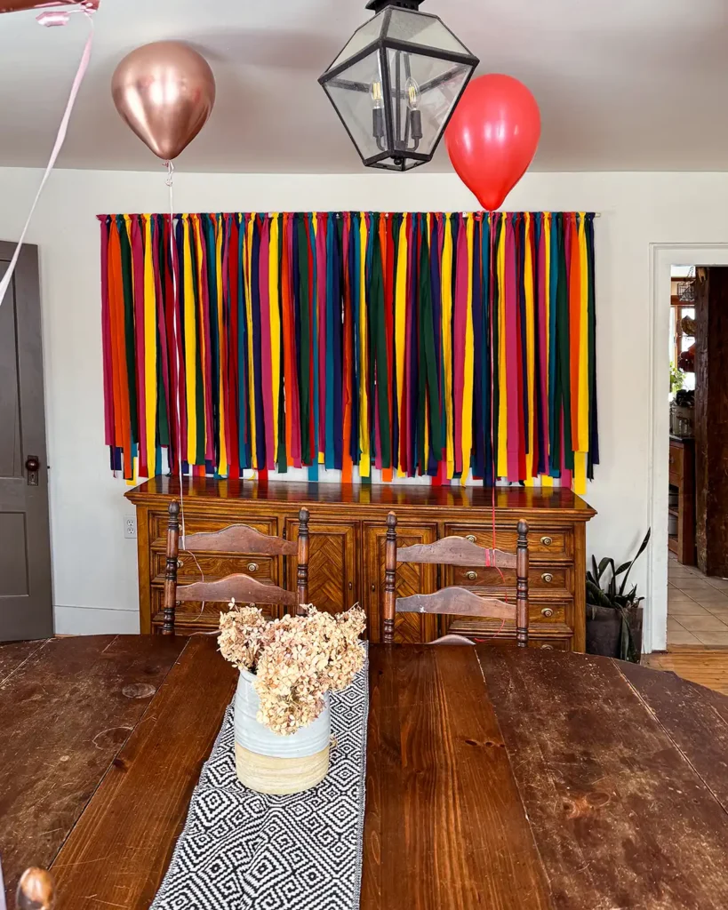 DIY backdrop for birthday parties made with wood dowels and fabric strips, hanging on a wall above a console in a dining room