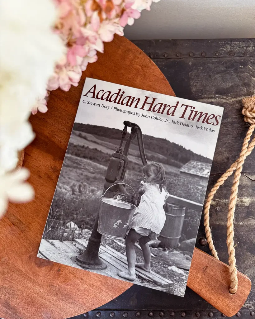 Acadian Hard Times paperback book sitting on a large bread board with hydrangeas peeking through