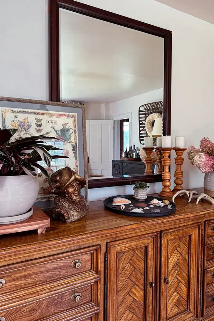 How to decorate a buffet table featured image with a large, wooden buffet filled with decor items including potted plants, vase of flowers, art, a large mirror, and more