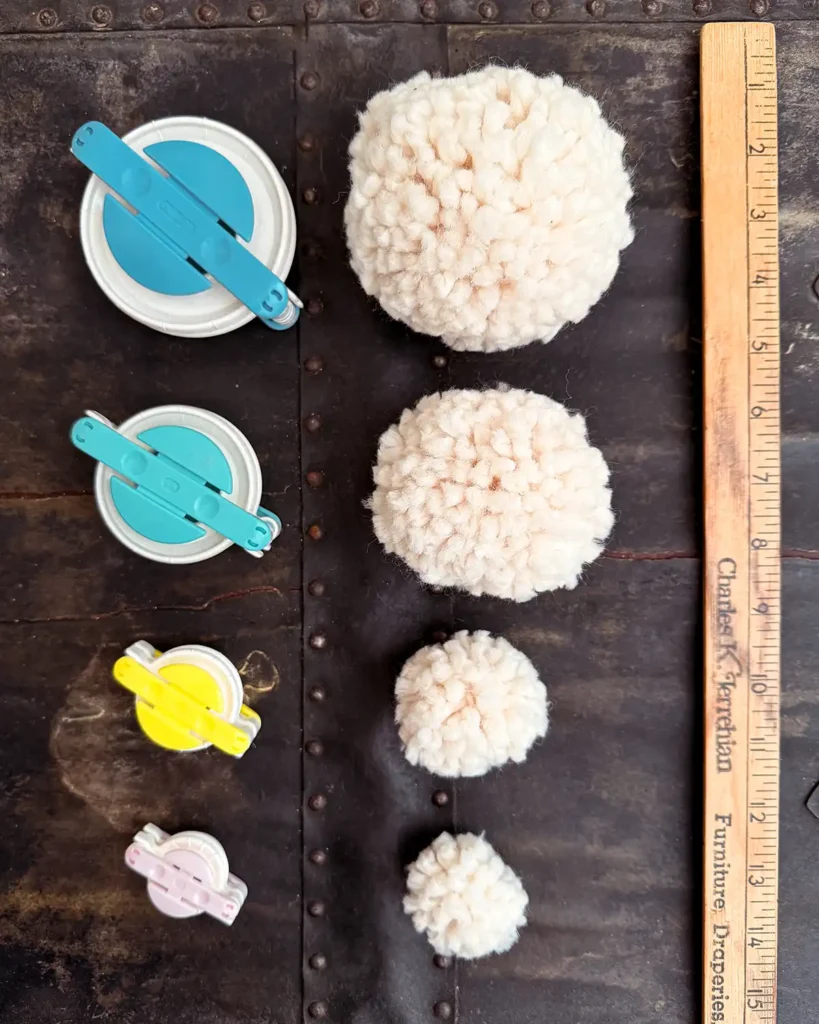 Different pom pom sizes made with different sized pom pom makers next to a ruler as a size guide