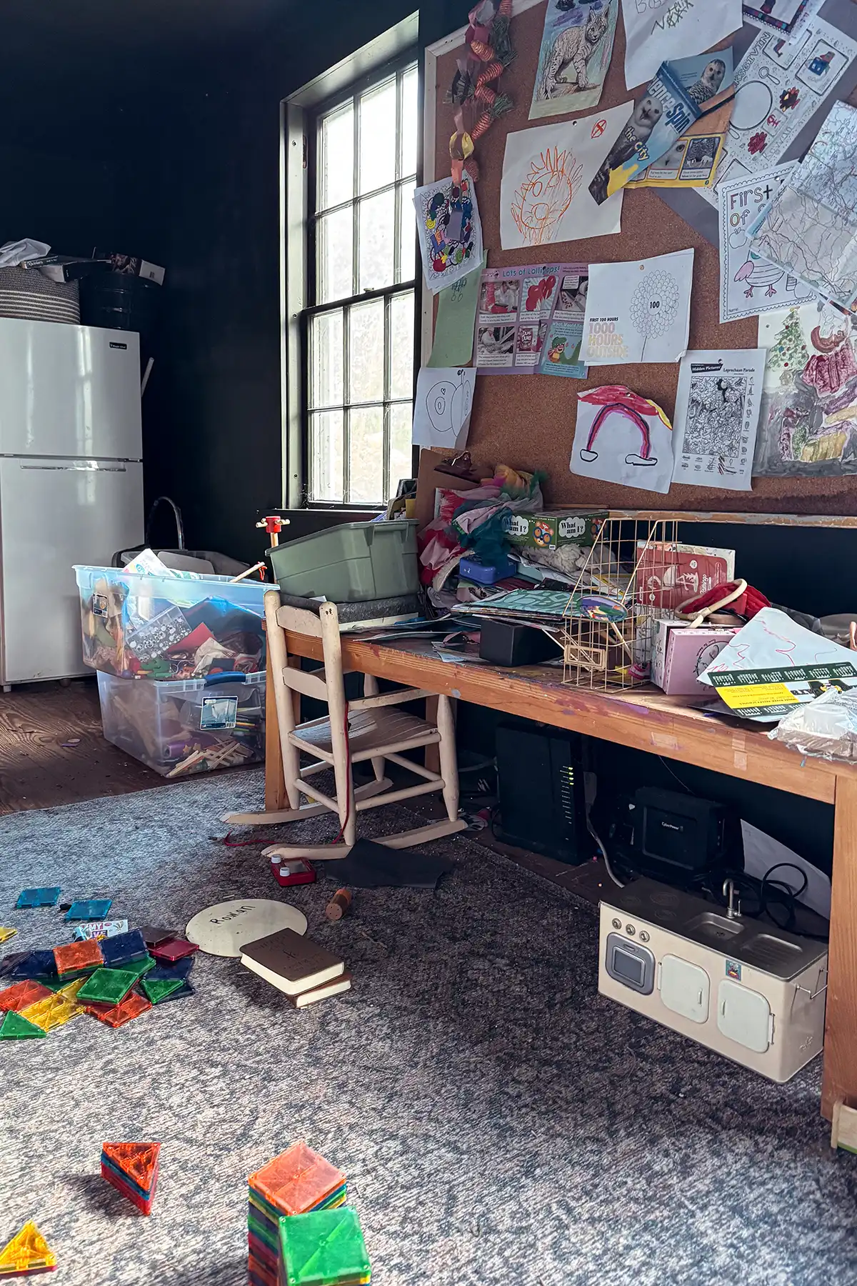 A messy playroom within a messy house with toys all over the floor and a craft table covered with toys and art supplies