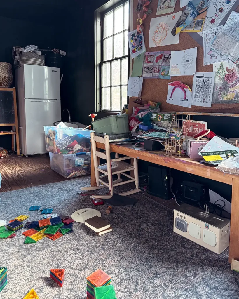 A messy playroom with toys littering the floor and an art desk completely covered with toys and art supplies