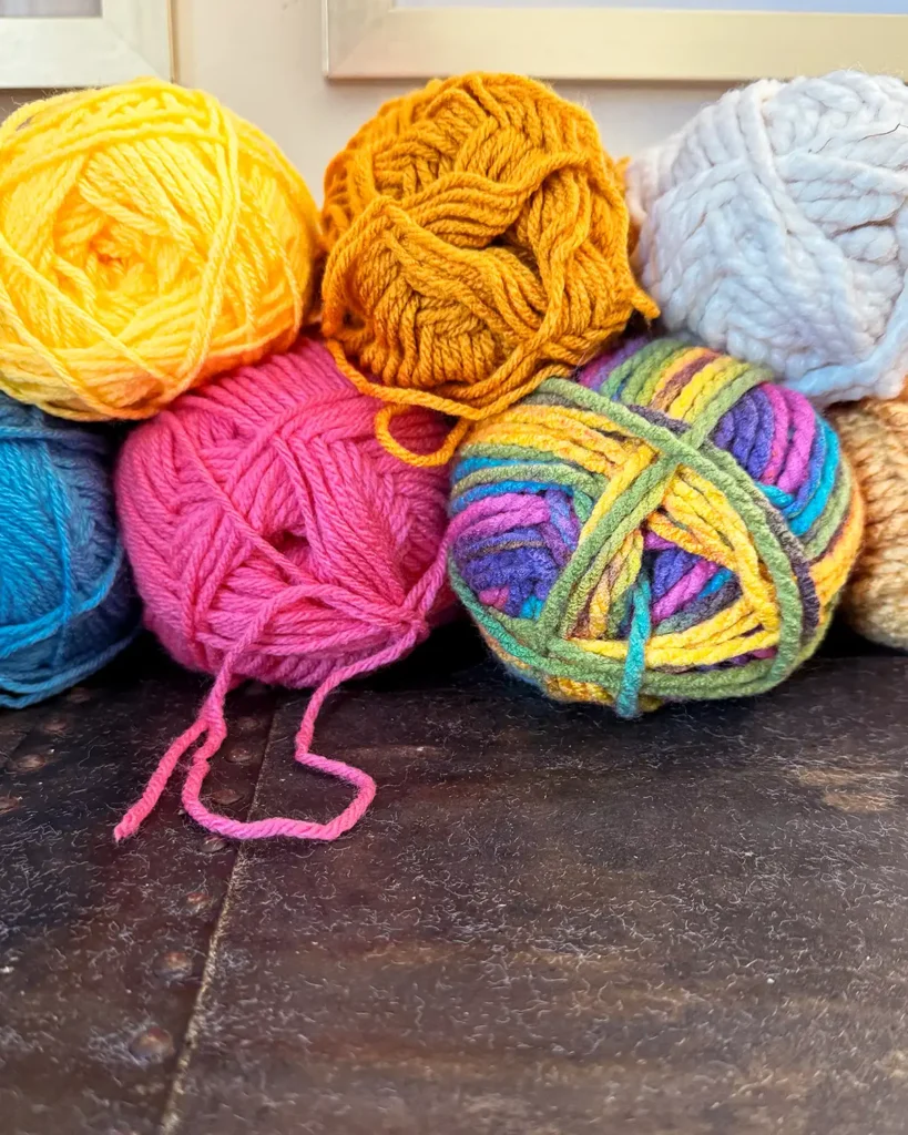 Stack of colorful yarn including yellow, mustard yellow, blue, pink, white, and variegated