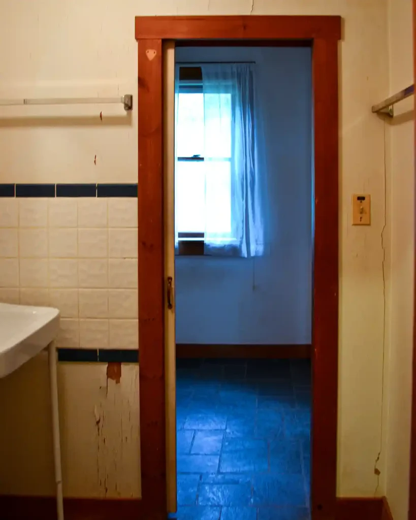 A dated bathroom on move-in day before beginning renovations, including a plywood pocket door and 70s style tile