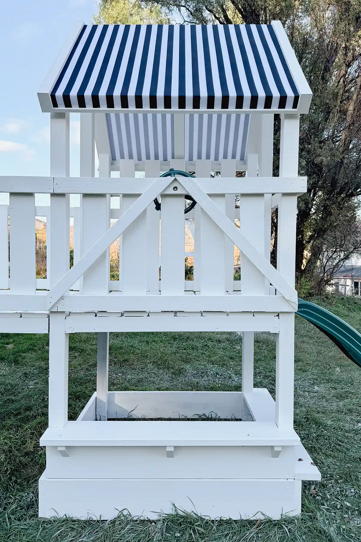 A black and white striped DIY playground canopy replacement for an old wooden playground that's painted white, sitting in a backyard