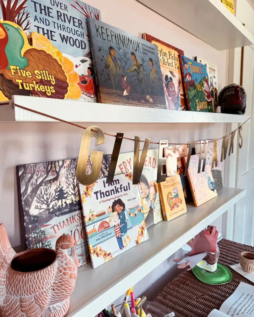 Kids bookshelves filled with Thanksgiving read alouds, a metallic "give thanks" banner, and ceramic turkey decor