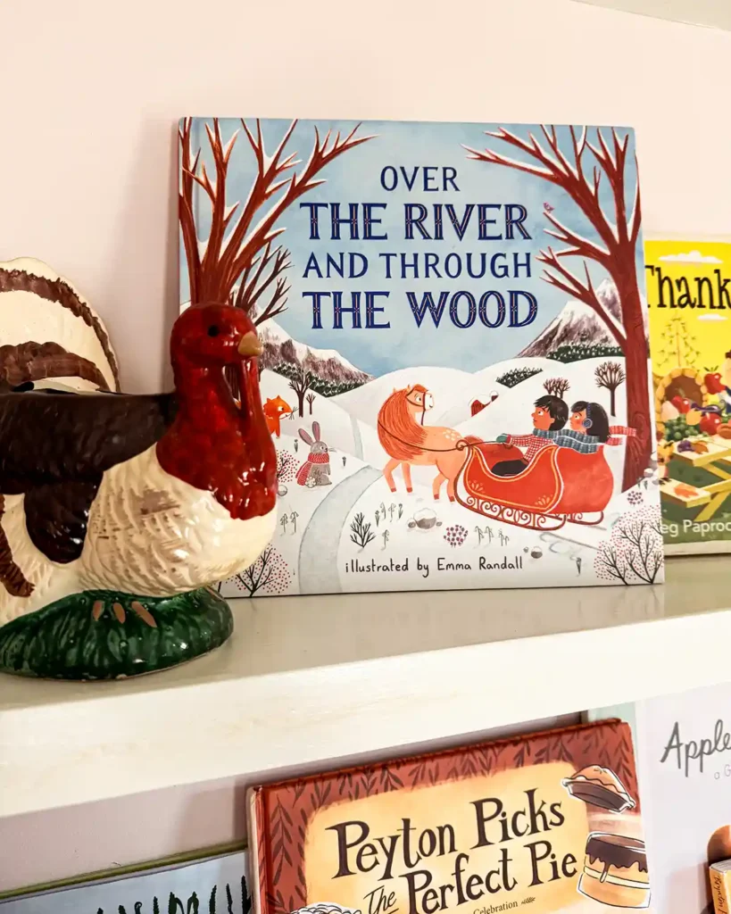 Over the River and Through the Woods picture book sitting on a child's bookshelf decorated for Thanksgiving with a ceramic turkey