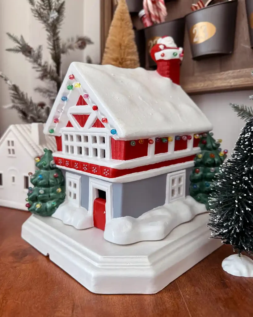 Ceramic Christmas house with Santa coming down the chimney and a Christmas tree in front surrounded by bottle brush trees