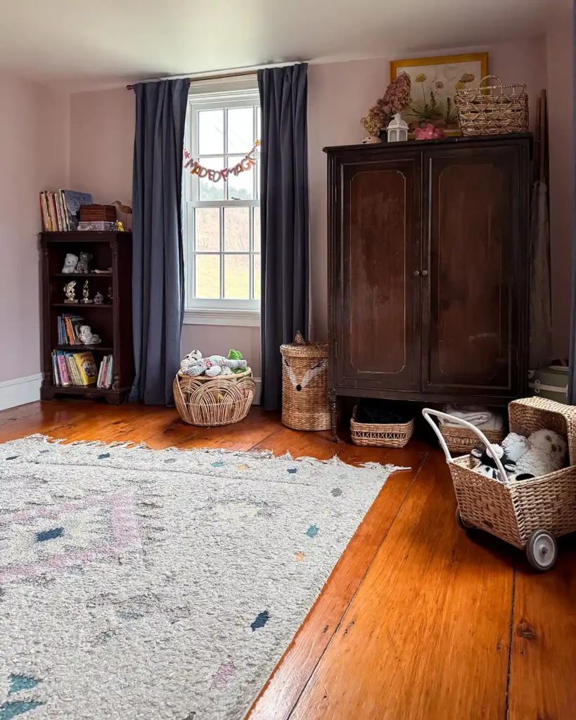 A tidy kids bedroom after cleaning up the mess with a large wardrobe with clean clothes put away, baskets of toys and stuffed animals where they belong and an organized bookshelf by the window