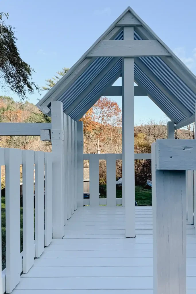 A DIY playground deck attached to a renovated, old playground to make a deck extension, playground painted white with a black and white striped canopy over the old section of the playground deck
