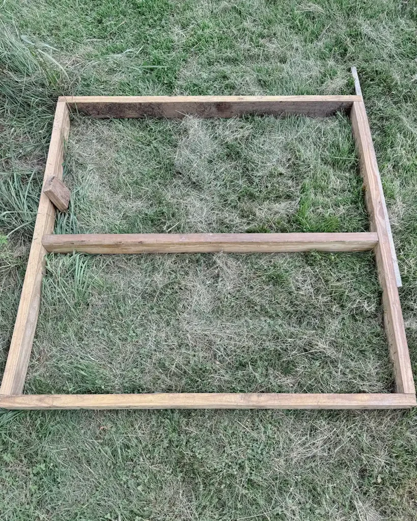 A DIY playground deck frame made from pressure treated 2" x 4" wood, a square frame with a middle joist sitting on the grass