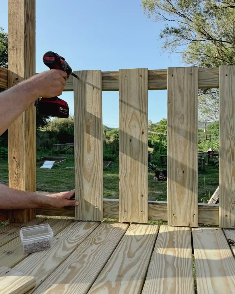 Installing balusters on our DIY playground deck extension using deck boards screwed into the railings a few inches apart