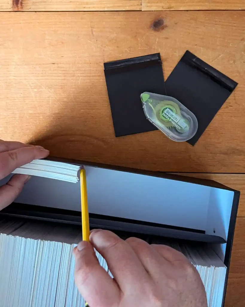 Placing a small stack of square photo prints inside a photo box and marking the edge with a pencil where the photo dividers will go