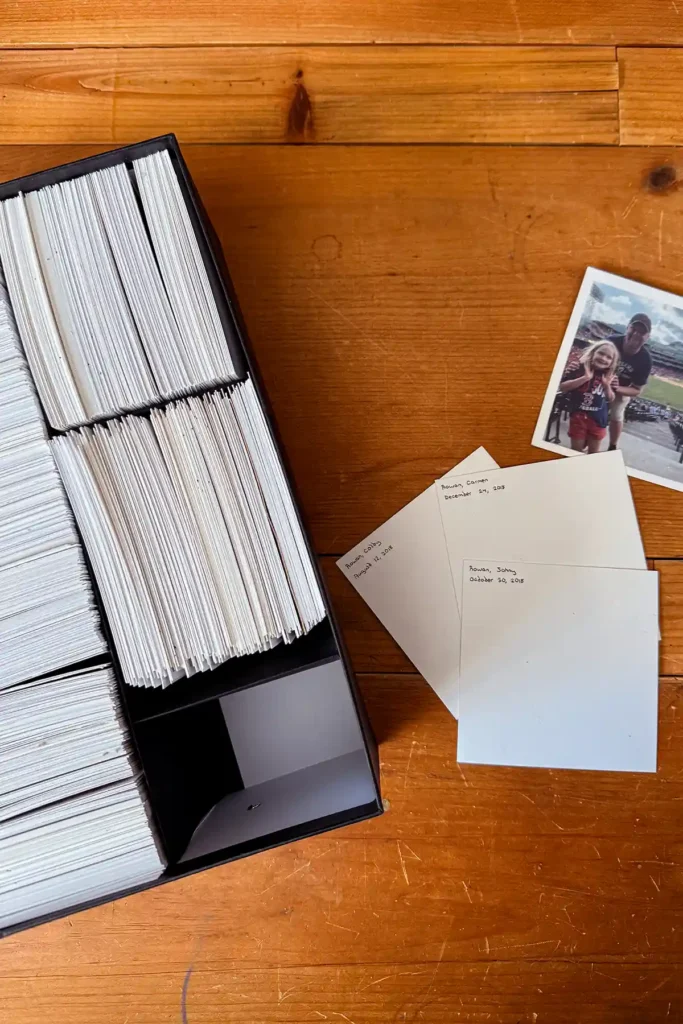 A standard black photo box modified to fit square photo prints is sitting open on a desktop with a collection of square photos, both front and back, scattered beside the box