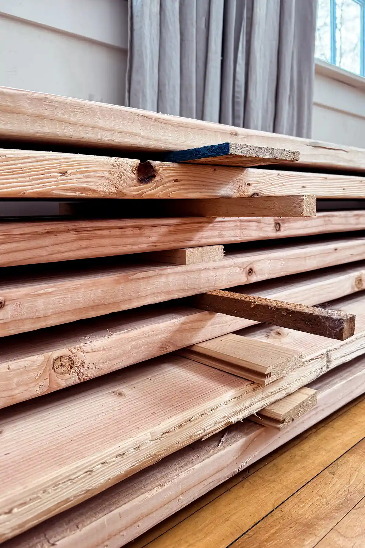A pile of rough cut lumber sitting in a dining room acclimating to the inside environment of the home; wood planks separated with shims between boards so each board can breathe