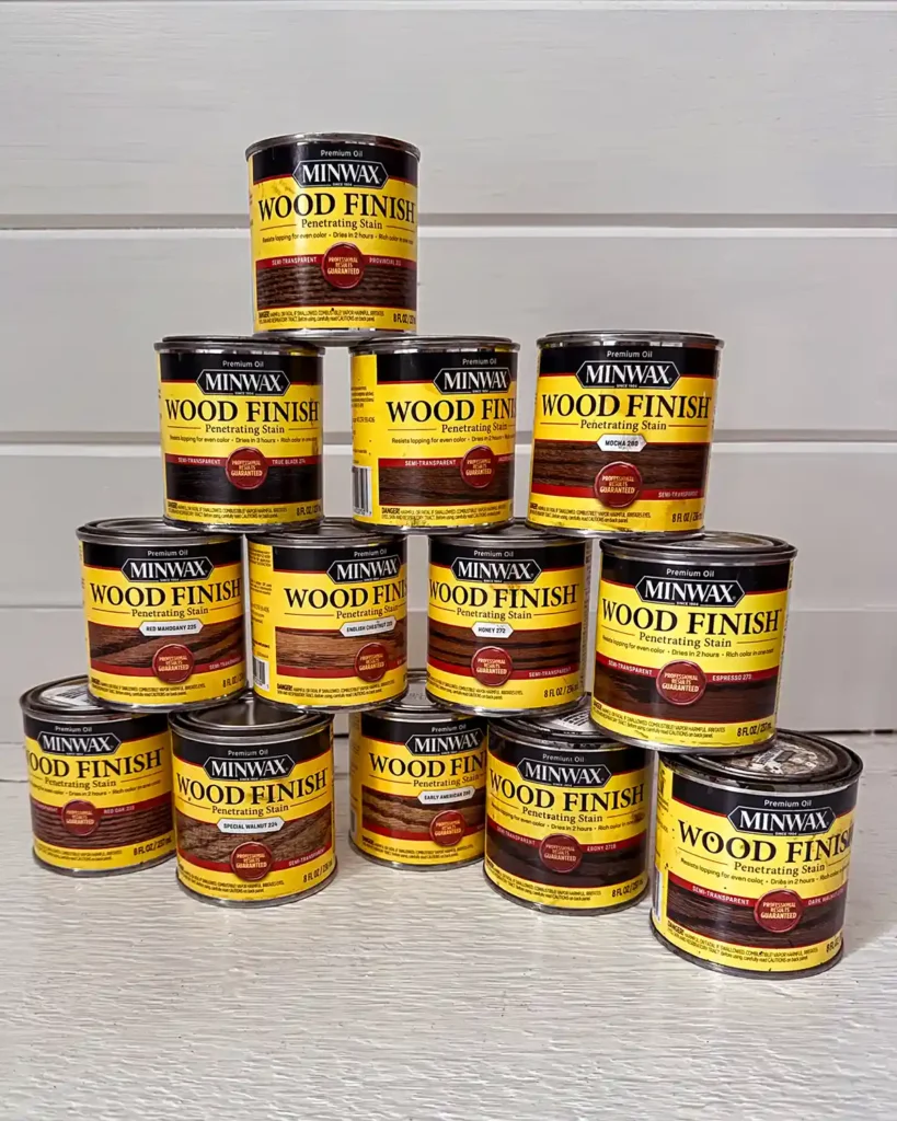 Thirteen sample pots of the darkest Minwax oil-based stains they provide stacked on top of each other in a white painted room