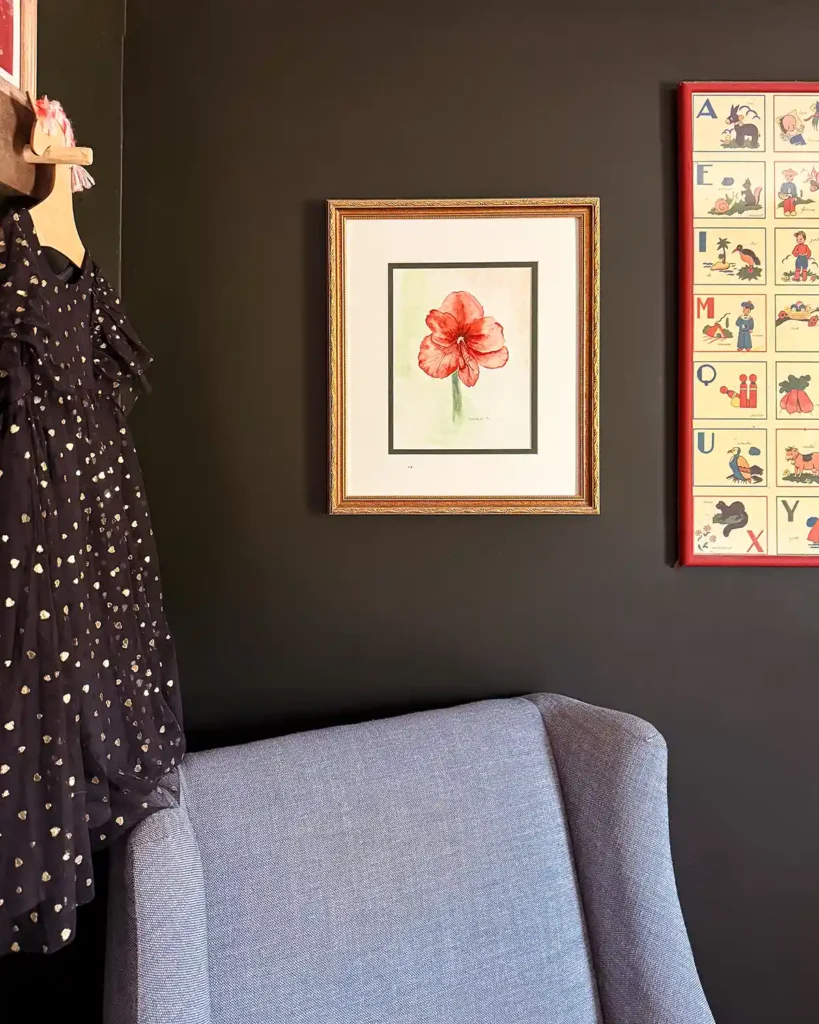 Framed, pink floral watercolor artwork hanging on dark nursery walls over a light blue glider