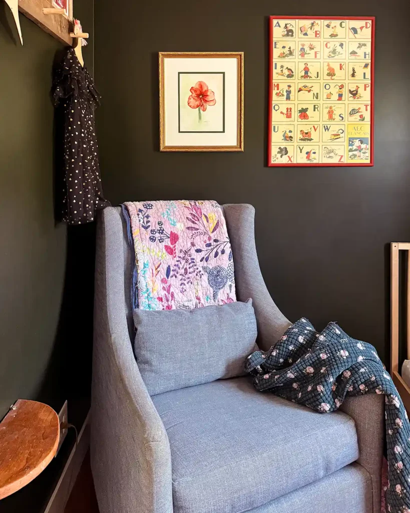 A pair of nursery art hanging on the wall above a glider; one of a watercolor floral and the other alphabet art