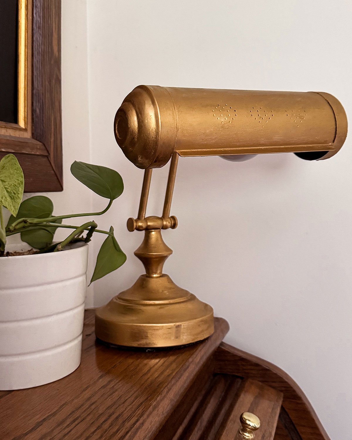 A DIY gold lamp makeover with a Rub N Buff finish; task lamp sitting on a small wooden rolltop desk next to a plant