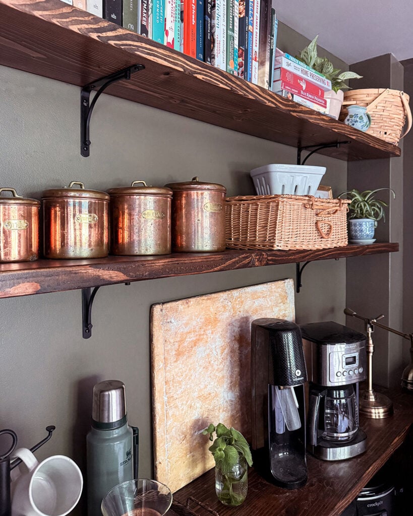 Open pantry shelves organized with kitchen items including a set of four copper canisters