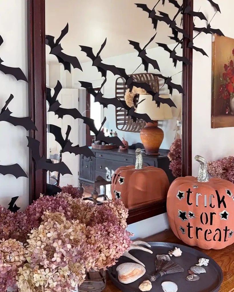 Black DIY paper bats hanging on a wall and mirror on top of a dining room buffet decorated for Halloween