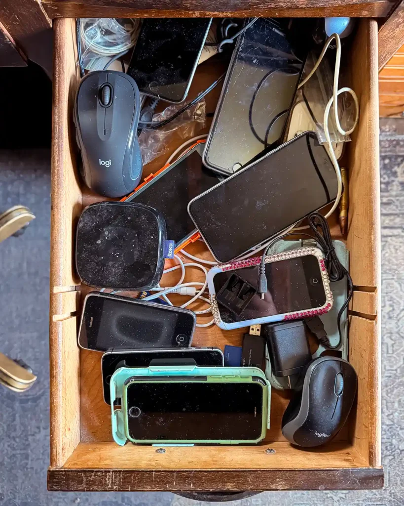 A desk drawer filled with old electronics including computer mice and old cell phones that need to be recycled