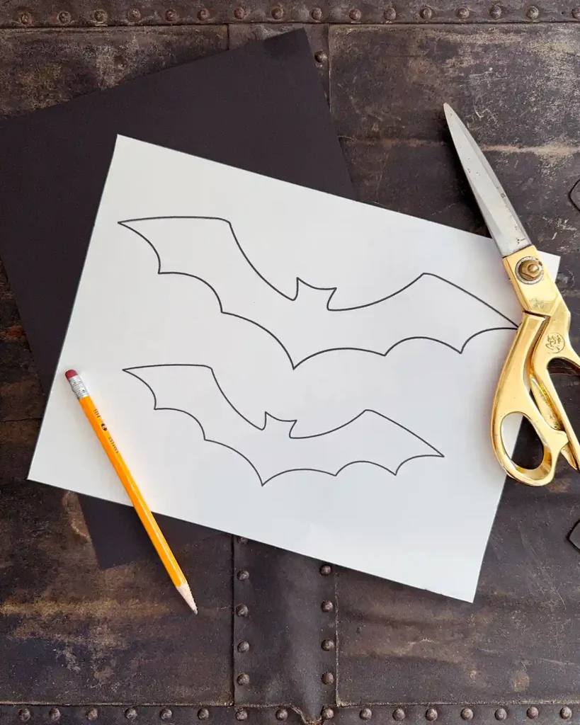 Halloween paper bat templates printed on white cardstock paper sitting on a table with scissors and a pencil