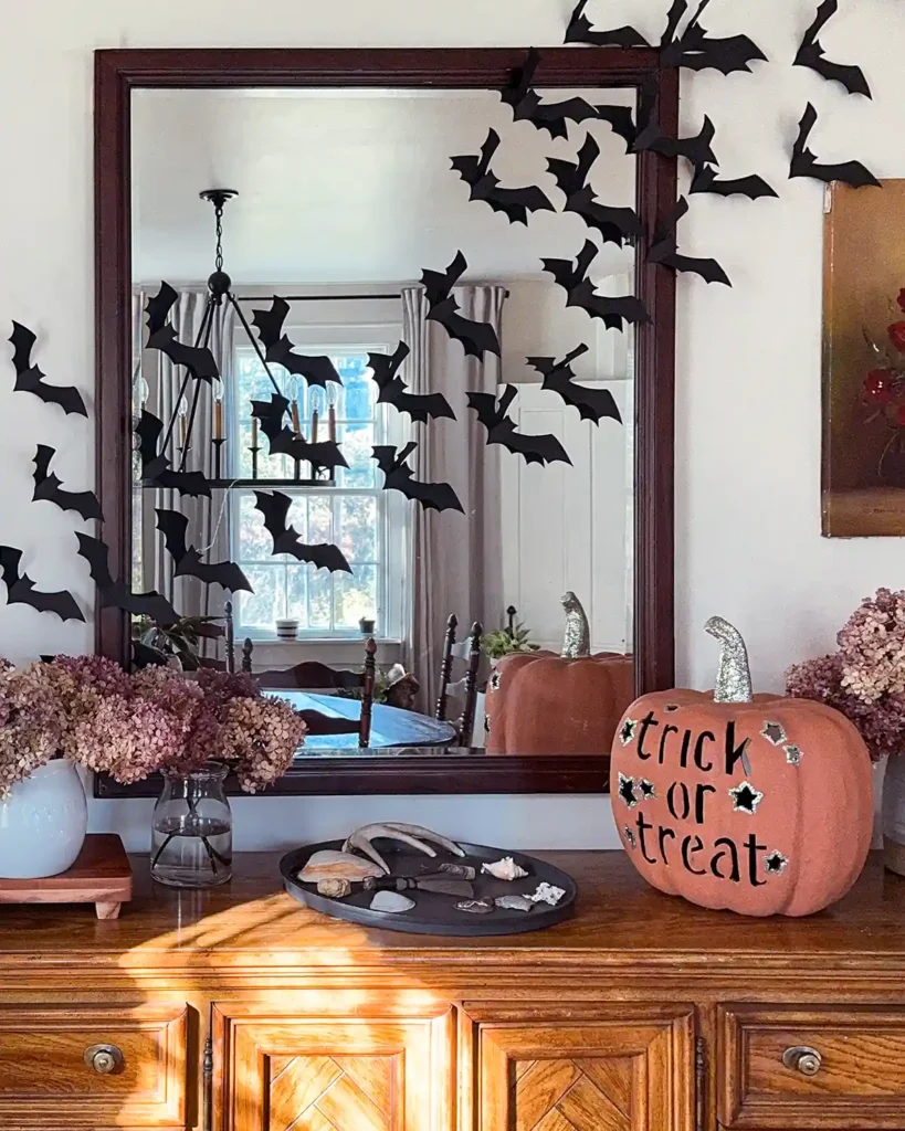 Homemade black paper bats hanging across a mirror and wall behind a dining room buffet for simple Halloween decor