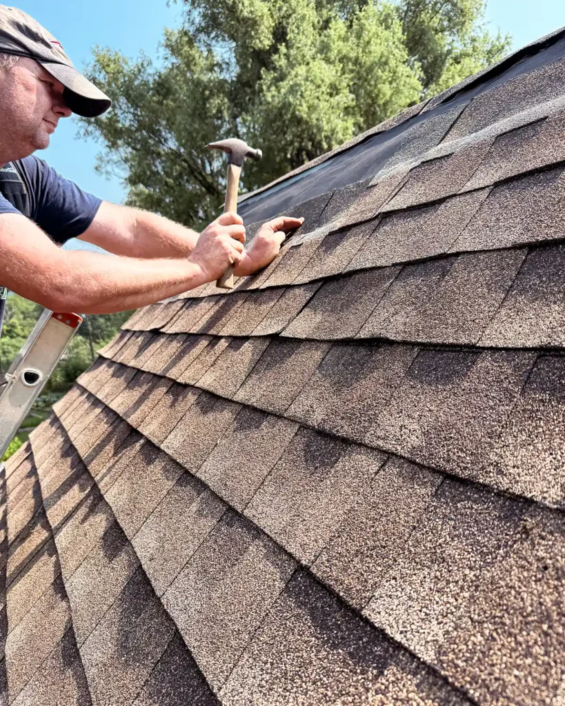 DIY shingling a shed roof nailing on brown asphalt shingles on a gable roof using a hammer and nails