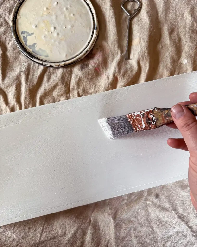 Applying multiple paint layers of glossy, white paint to a shelf using a paint brush