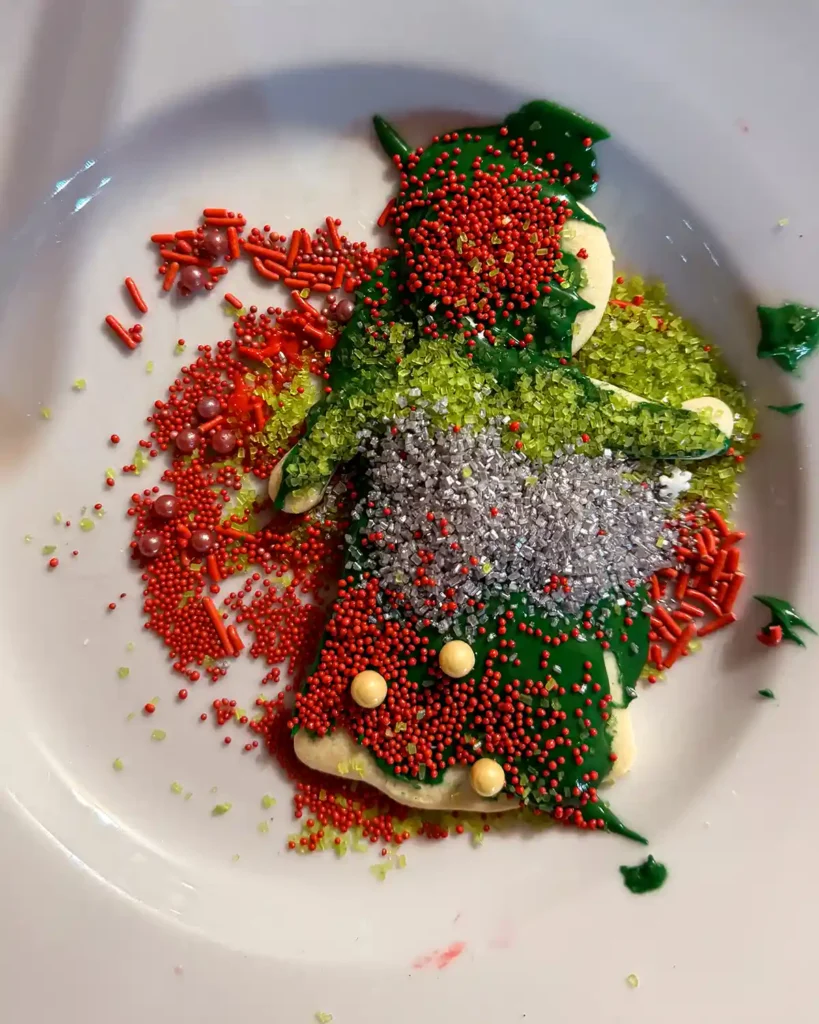 A Christmas angel sugar cookie with excessive amounts of red, green, and silver sprinkles, sitting on a plate