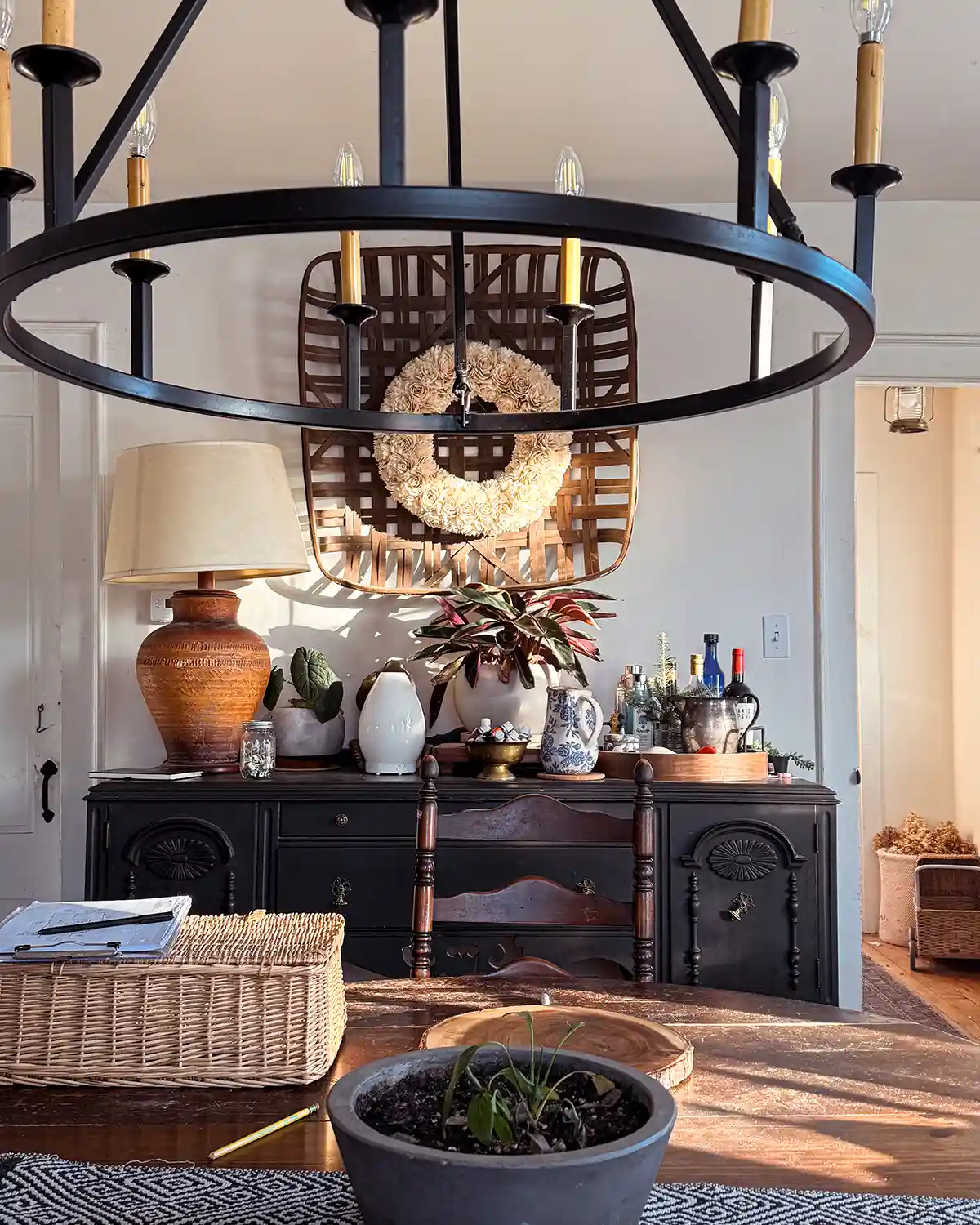 A dining room light fixture hanging over a table with a buffet in the background with light streaming through