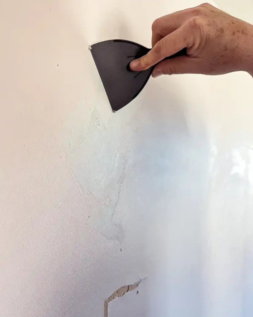 Applying the first coat of joint compound with a putty knife to repair damaged drywall
