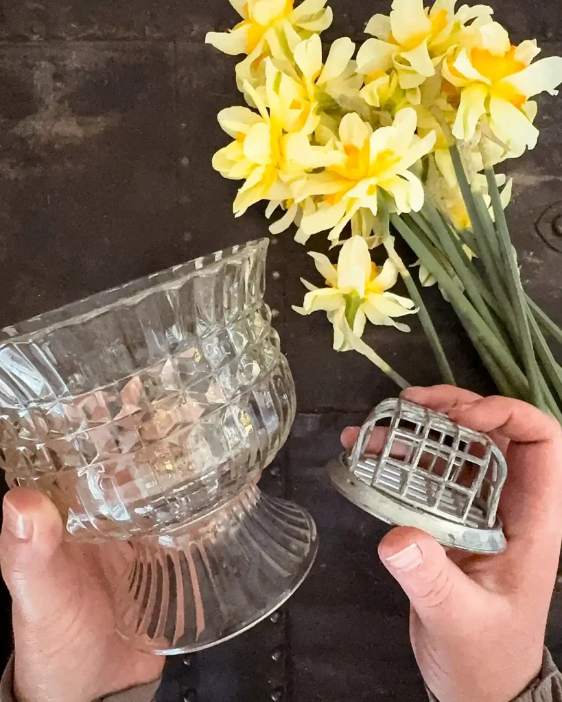 Choosing supplies for a floral arrangement including a selection of white and yellow daffodils, footed clear glass bowl, and vintage metal cage floral frog