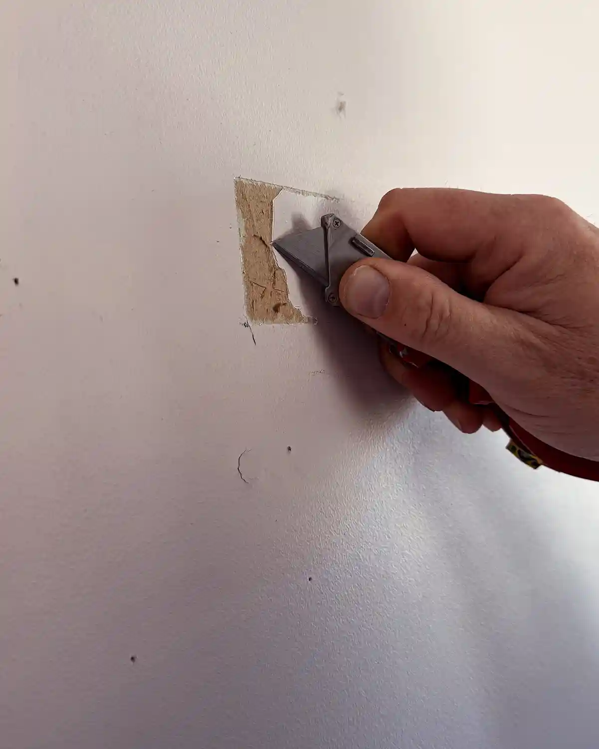 Cutting the peeling parts of the drywall with a utility knife to prepare the surface for patching