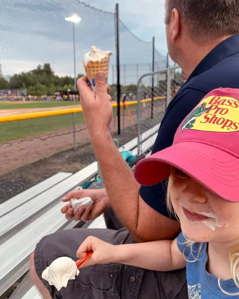 Dad and daughter enjoying ice cream cones at the ballpark at dusk