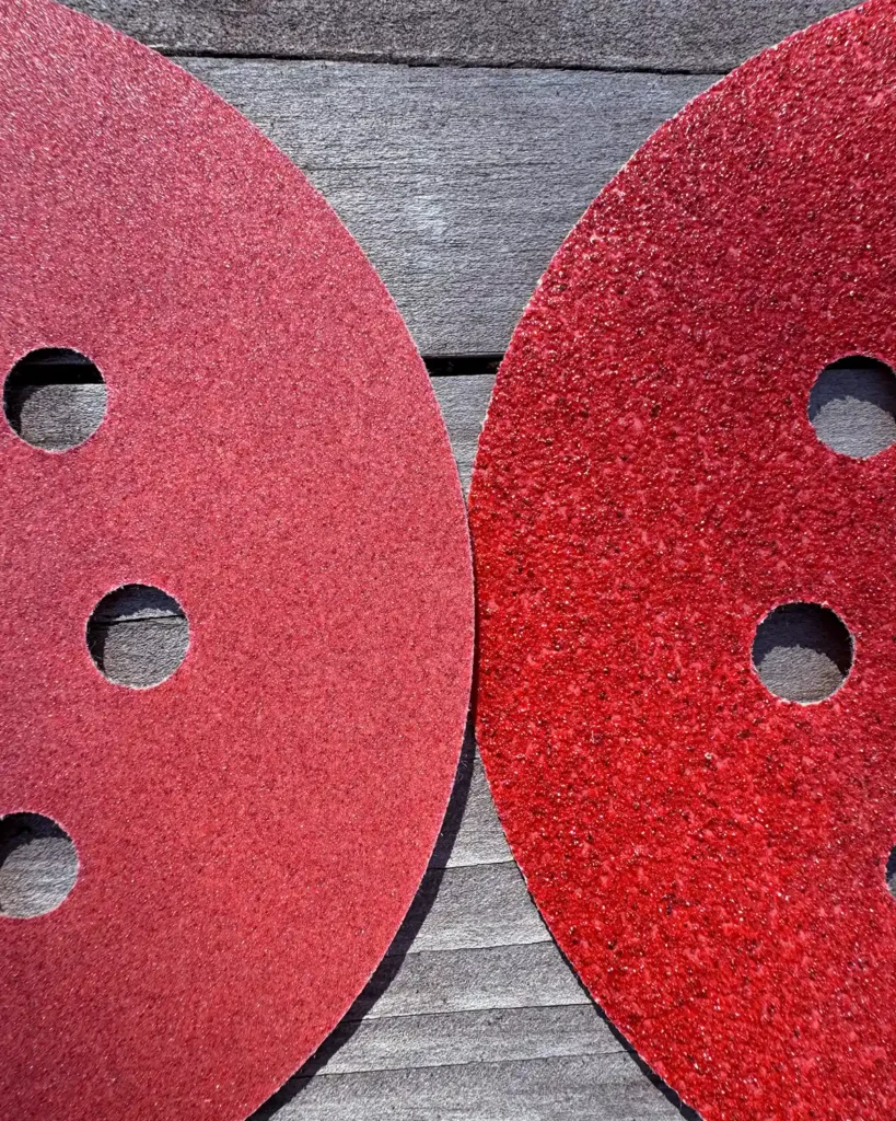 A fine-grit orbital sander disc on the left compared to a coarse-grit disc on the right